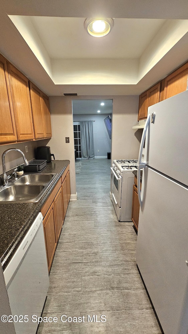 kitchen featuring white appliances, a tray ceiling, sink, and light wood-type flooring