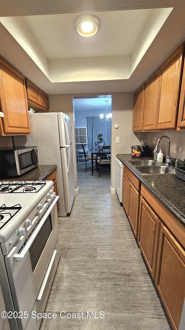 kitchen with sink, an inviting chandelier, white appliances, and a tray ceiling