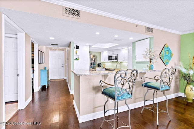 kitchen featuring dark wood-type flooring, a breakfast bar, white cabinetry, kitchen peninsula, and light stone countertops