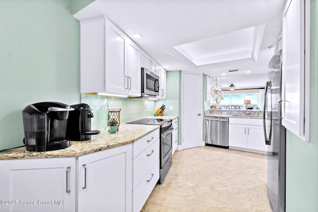 kitchen featuring appliances with stainless steel finishes, tasteful backsplash, a tray ceiling, light stone countertops, and white cabinets