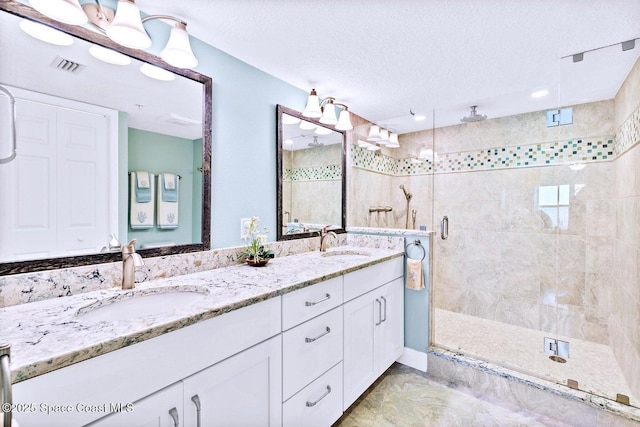 bathroom with a textured ceiling, double vanity, a stall shower, and a sink