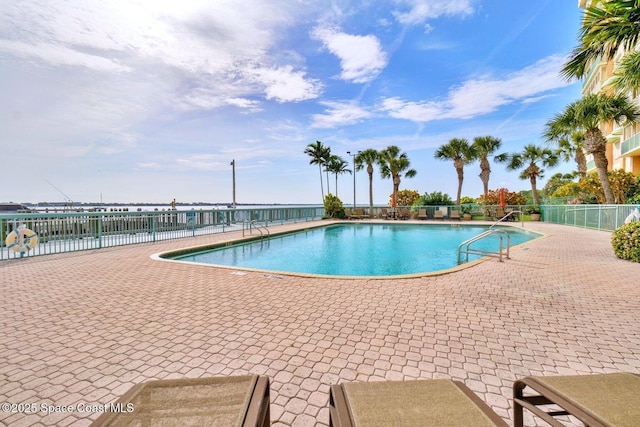 community pool featuring a water view, a patio area, and fence