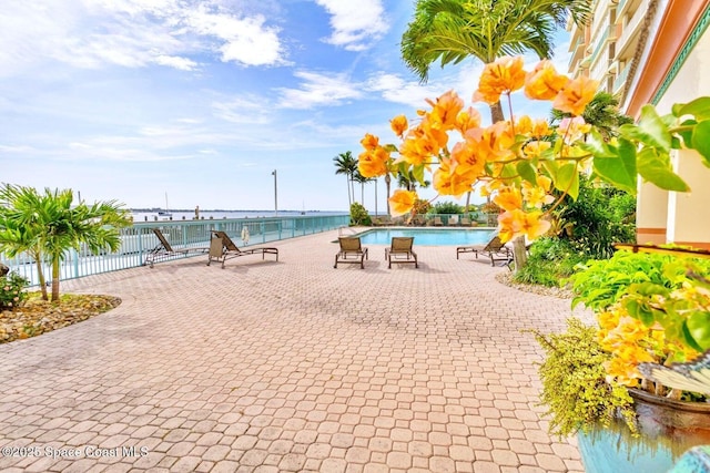 view of pool featuring a water view, a patio area, and fence