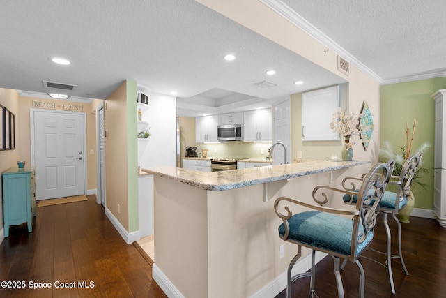 kitchen featuring visible vents, appliances with stainless steel finishes, dark wood-type flooring, a peninsula, and white cabinetry