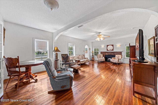 living room featuring ceiling fan, hardwood / wood-style flooring, a fireplace, and a textured ceiling