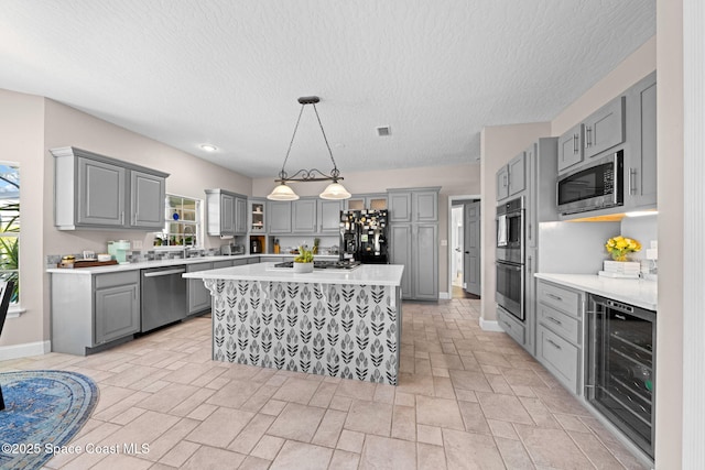 kitchen with a kitchen island, decorative light fixtures, gray cabinetry, wine cooler, and stainless steel appliances