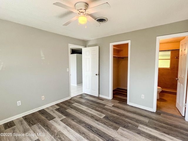 unfurnished bedroom with ensuite bathroom, a spacious closet, ceiling fan, dark wood-type flooring, and a closet