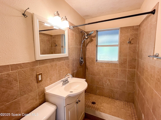 bathroom with a tile shower, vanity, tile walls, and toilet