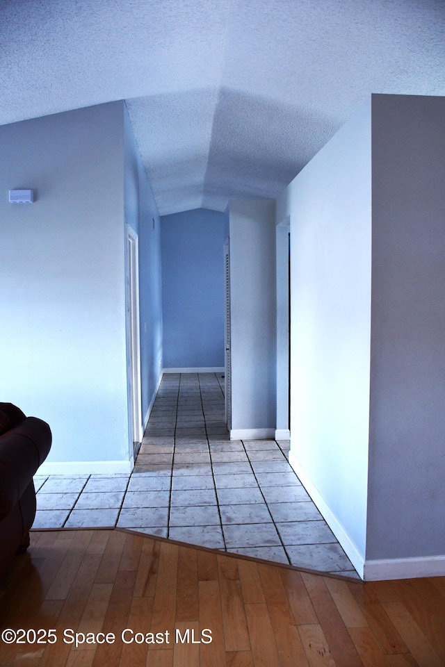 corridor with lofted ceiling, hardwood / wood-style flooring, and a textured ceiling