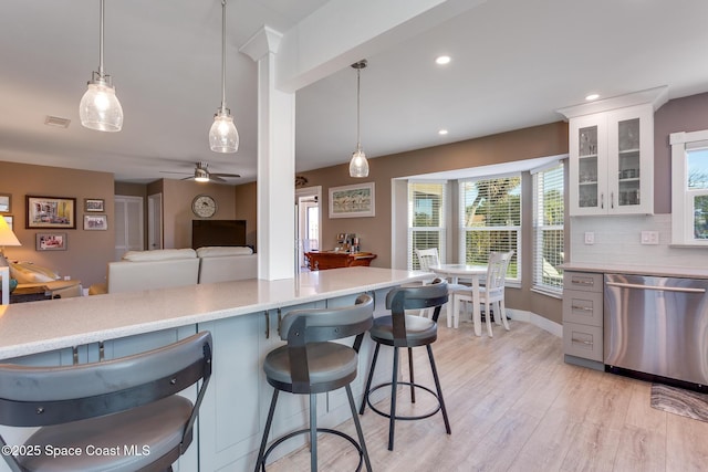 kitchen with pendant lighting, white cabinetry, a breakfast bar area, stainless steel dishwasher, and light hardwood / wood-style floors