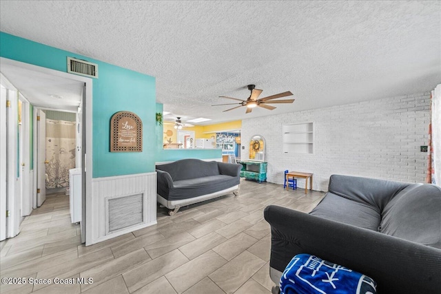 living room with ceiling fan, a textured ceiling, and brick wall