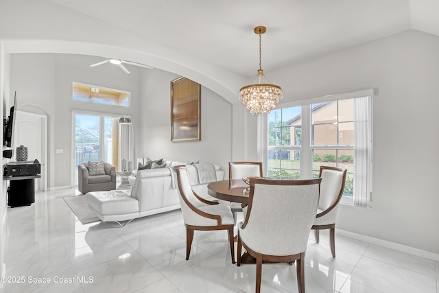 dining area with baseboards, arched walkways, vaulted ceiling, ceiling fan with notable chandelier, and marble finish floor