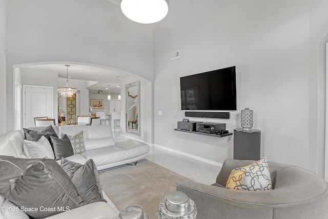 living area with visible vents, a notable chandelier, arched walkways, baseboards, and a towering ceiling