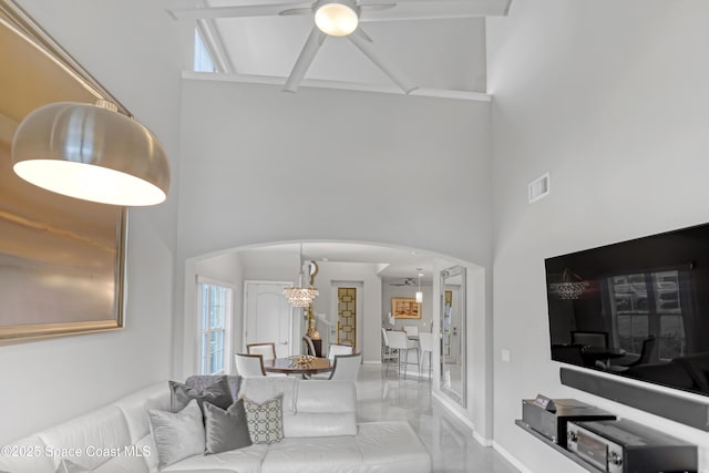 living area with visible vents, arched walkways, a towering ceiling, and a ceiling fan