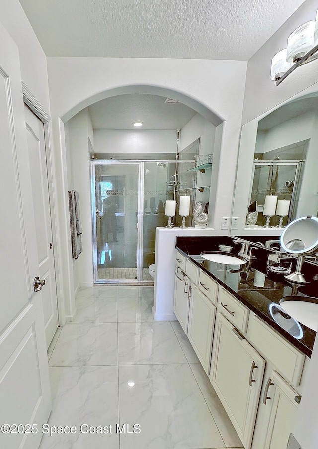 bathroom featuring double vanity, a stall shower, a sink, toilet, and marble finish floor