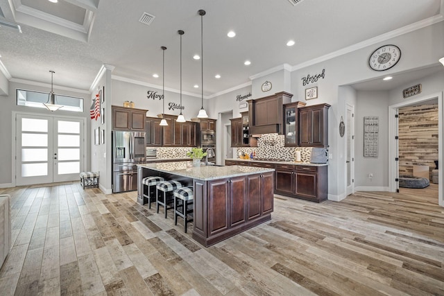 kitchen featuring appliances with stainless steel finishes, decorative light fixtures, a breakfast bar area, a kitchen island with sink, and dark brown cabinets