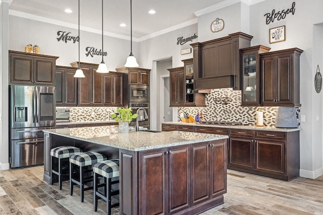 kitchen with pendant lighting, sink, appliances with stainless steel finishes, dark brown cabinetry, and a center island with sink