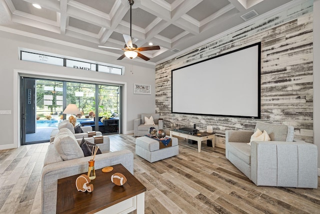 cinema with light hardwood / wood-style flooring, a high ceiling, coffered ceiling, ornamental molding, and beamed ceiling