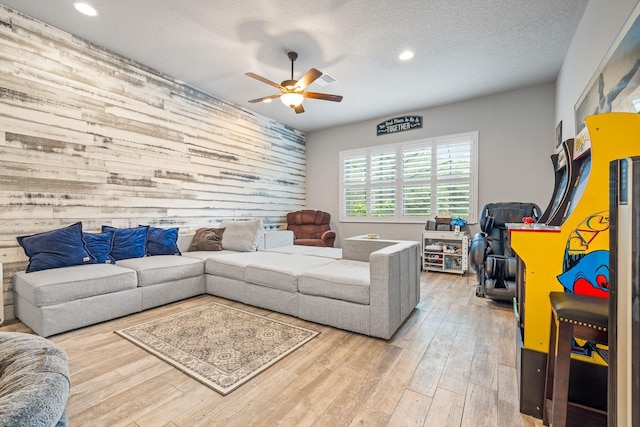 living room featuring ceiling fan, hardwood / wood-style floors, a textured ceiling, and wood walls