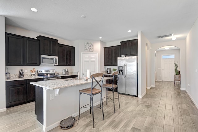 kitchen with sink, light stone counters, appliances with stainless steel finishes, a kitchen breakfast bar, and a kitchen island with sink