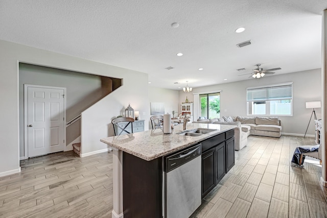 kitchen with sink, dishwasher, light stone counters, a textured ceiling, and a center island with sink