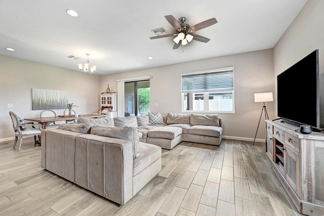 living room with ceiling fan with notable chandelier, light wood-type flooring, and a wealth of natural light