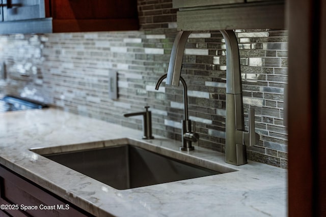 room details with sink, decorative backsplash, and light stone countertops