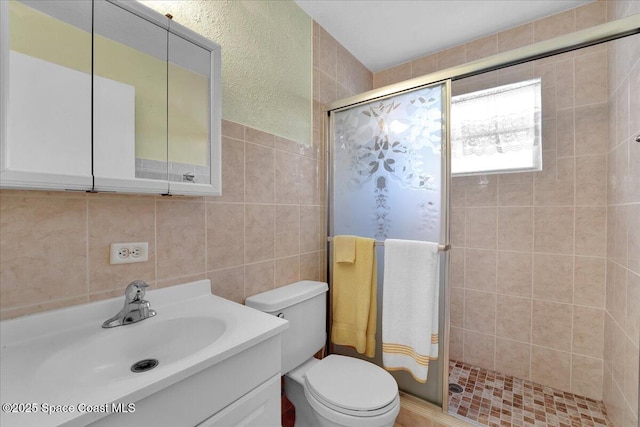 bathroom with a shower with door, vanity, tile walls, and toilet