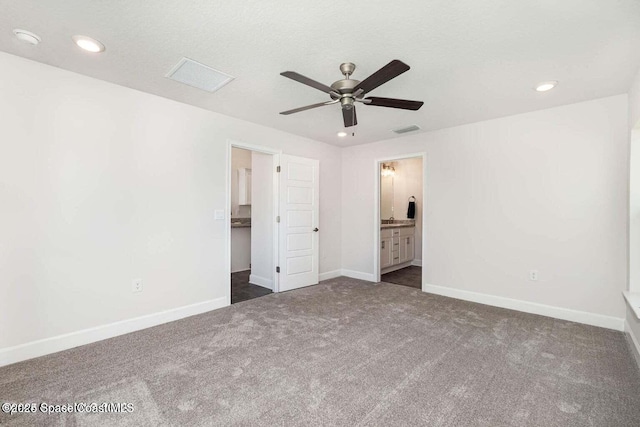 unfurnished bedroom featuring dark colored carpet, a spacious closet, connected bathroom, and ceiling fan