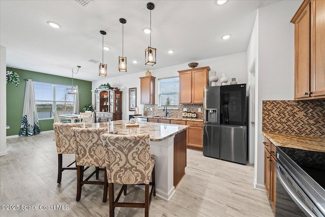 kitchen with a breakfast bar area, a center island, stainless steel fridge with ice dispenser, hanging light fixtures, and light stone countertops