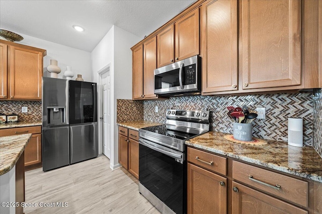 kitchen with tasteful backsplash, appliances with stainless steel finishes, light stone countertops, and light wood-type flooring