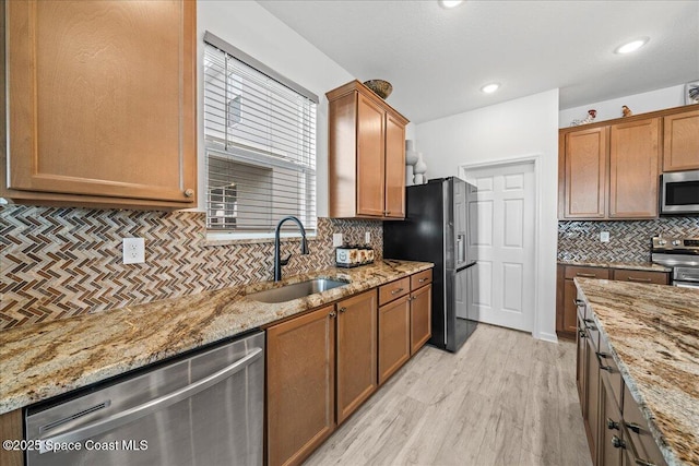 kitchen featuring light stone counters, appliances with stainless steel finishes, light hardwood / wood-style floors, and sink