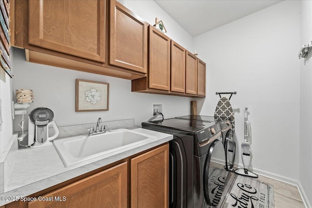 laundry room with cabinets, washer and clothes dryer, sink, and light hardwood / wood-style flooring