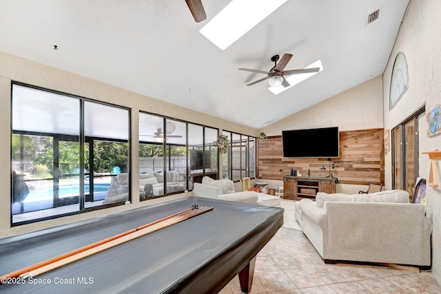 living area featuring visible vents, vaulted ceiling with skylight, light tile patterned flooring, ceiling fan, and wood walls