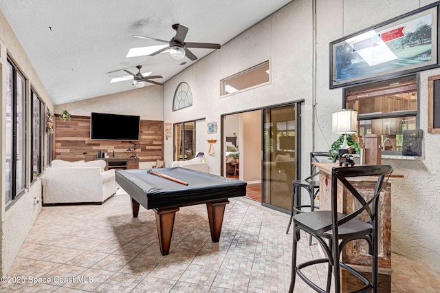 rec room featuring high vaulted ceiling, billiards, a skylight, ceiling fan, and a textured wall