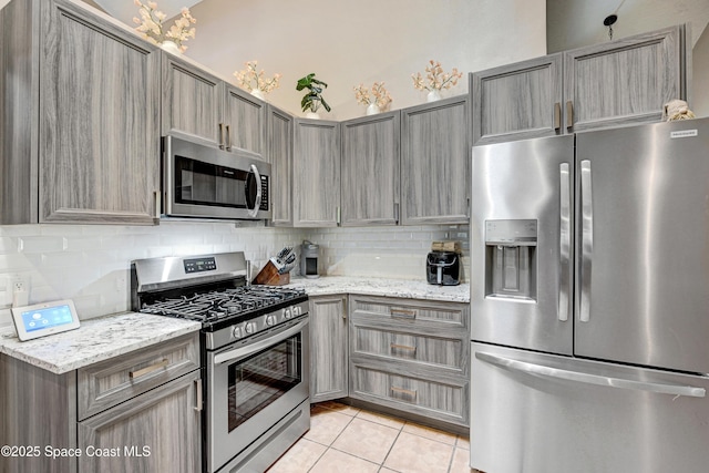 kitchen with light tile patterned floors, light stone countertops, tasteful backsplash, and stainless steel appliances