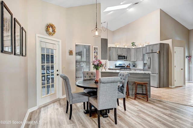 dining room with a skylight, light wood-style flooring, baseboards, and high vaulted ceiling