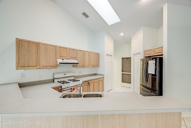 kitchen featuring sink, light brown cabinetry, black refrigerator, white range with gas cooktop, and kitchen peninsula