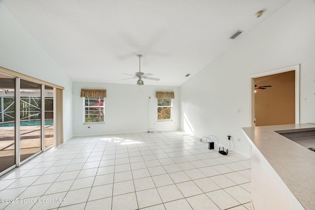 empty room with a textured ceiling, vaulted ceiling, ceiling fan, and light tile patterned flooring