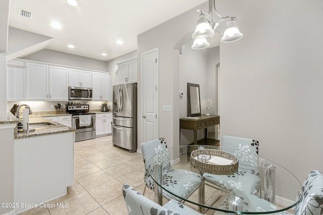 kitchen with sink, light stone counters, hanging light fixtures, stainless steel appliances, and white cabinets