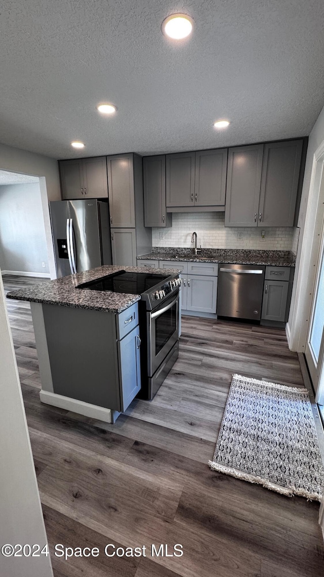 kitchen with dark stone countertops, dark hardwood / wood-style flooring, gray cabinets, stainless steel appliances, and decorative backsplash