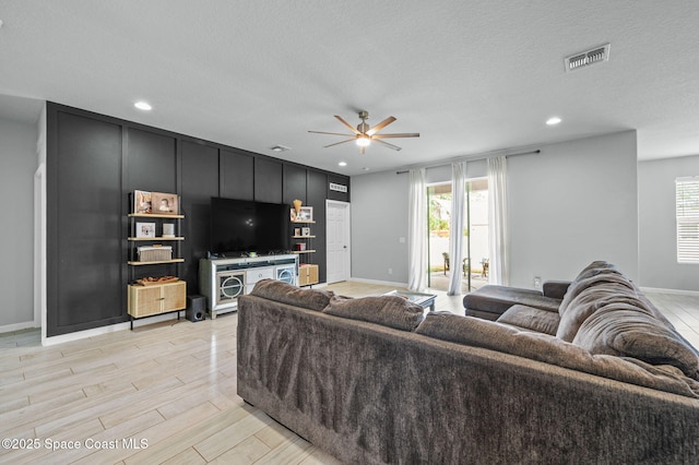 living room with ceiling fan, light hardwood / wood-style floors, and a textured ceiling