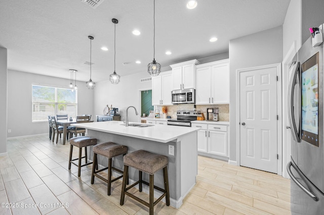 kitchen with sink, hanging light fixtures, stainless steel appliances, white cabinets, and a center island with sink