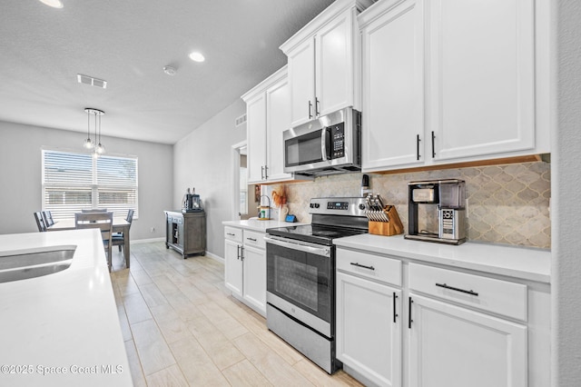 kitchen featuring hanging light fixtures, light wood-type flooring, appliances with stainless steel finishes, white cabinets, and backsplash