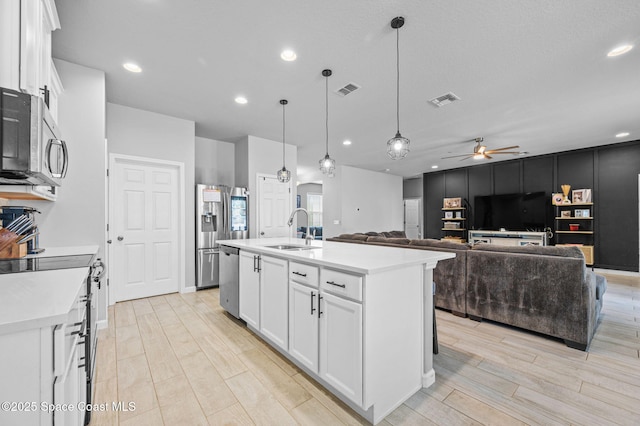 kitchen with sink, decorative light fixtures, white cabinets, and a center island with sink