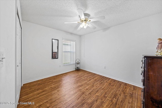 unfurnished bedroom with a textured ceiling, baseboards, and wood finished floors