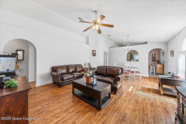 living room with arched walkways, light wood-style flooring, vaulted ceiling, ceiling fan, and a textured ceiling