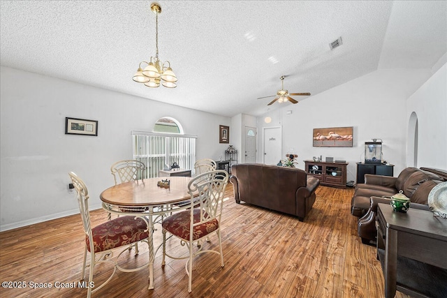 dining room featuring arched walkways, lofted ceiling, ceiling fan with notable chandelier, wood finished floors, and visible vents