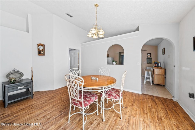 dining area featuring visible vents, vaulted ceiling, a textured ceiling, light wood-type flooring, and a chandelier