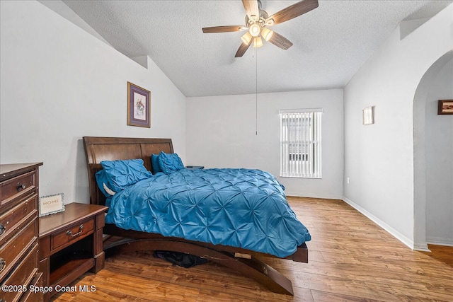 bedroom with arched walkways, vaulted ceiling, a textured ceiling, wood finished floors, and baseboards